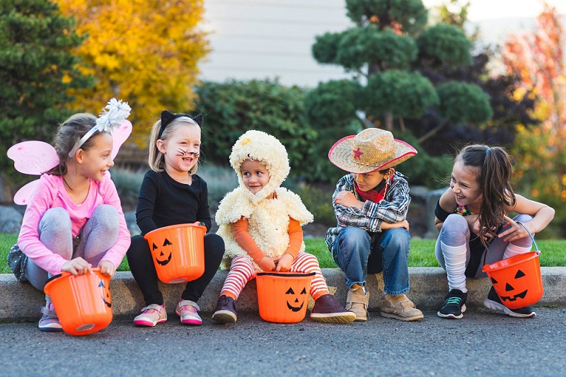 Kids sitting on a curb dressed up for halloween and ready to go trunk-or-treating