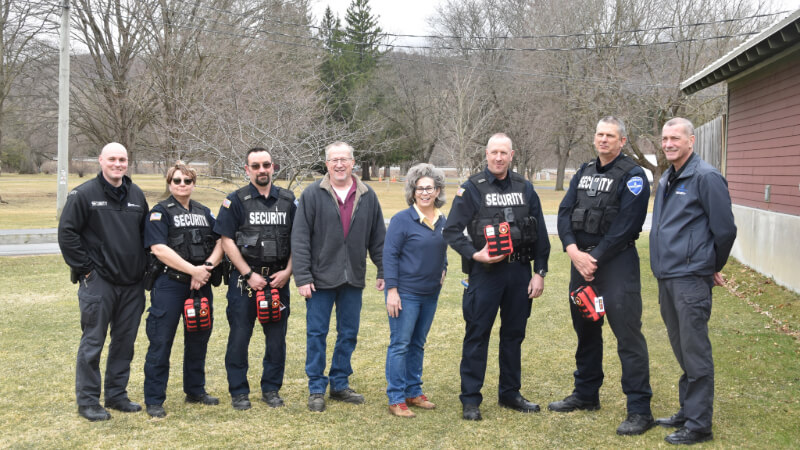 Eight people pose for a photo. Four of them are wearing security officer attire and holding red medic kits.