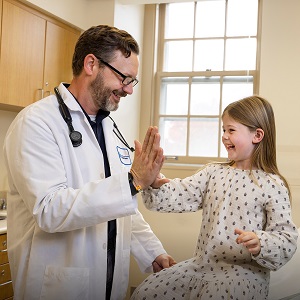 Dr. Brandon Greene high-fiving and smiling with pediatric patient