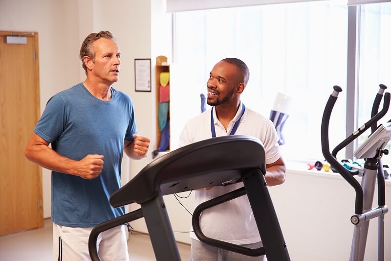 Patient undergoing cardiac rehab by exercising on a treadmill with a heart specialist supervising
