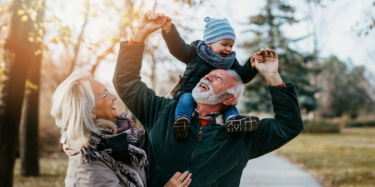 grandparents playing with toddler grandchild outside, all smiling