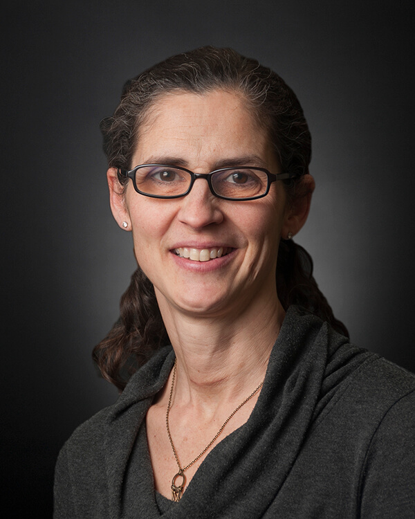 A woman is photographed from the shoulders up. She is wearing professional attire.