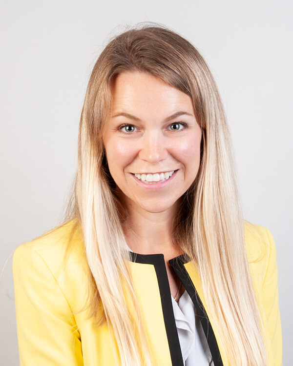 A woman is photographed from the shoulders up. She is wearing professional attire.