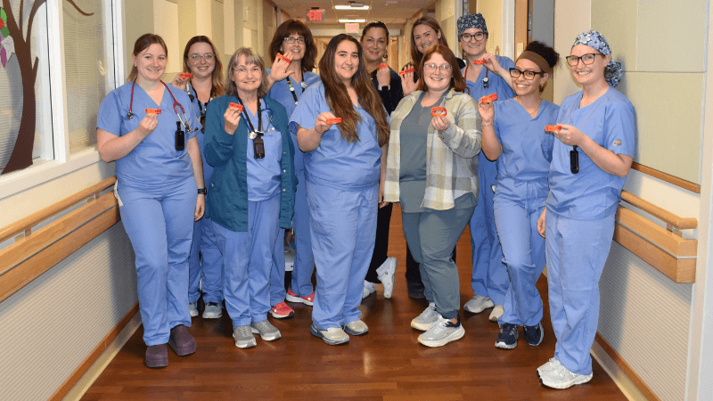 A group of 11 caregivers stand in a hospital hallway. They are each holding a health alert wristband. 