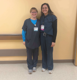 Two women dressed in hospital scrubs are photographed standing next to each other.