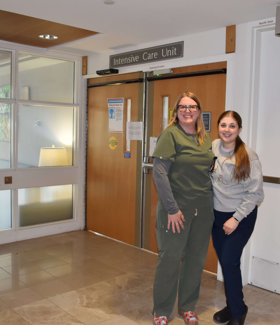 Two women stand togehter inside a hospital outside a door that says Intensive Care Unit.